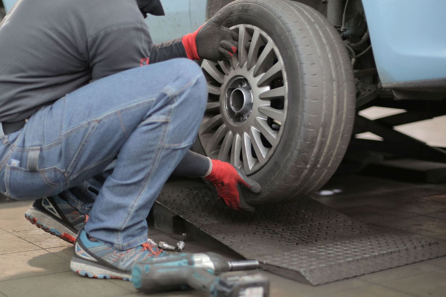 Mechanic changing a car tire indoors, using tools for vehicle maintenance.