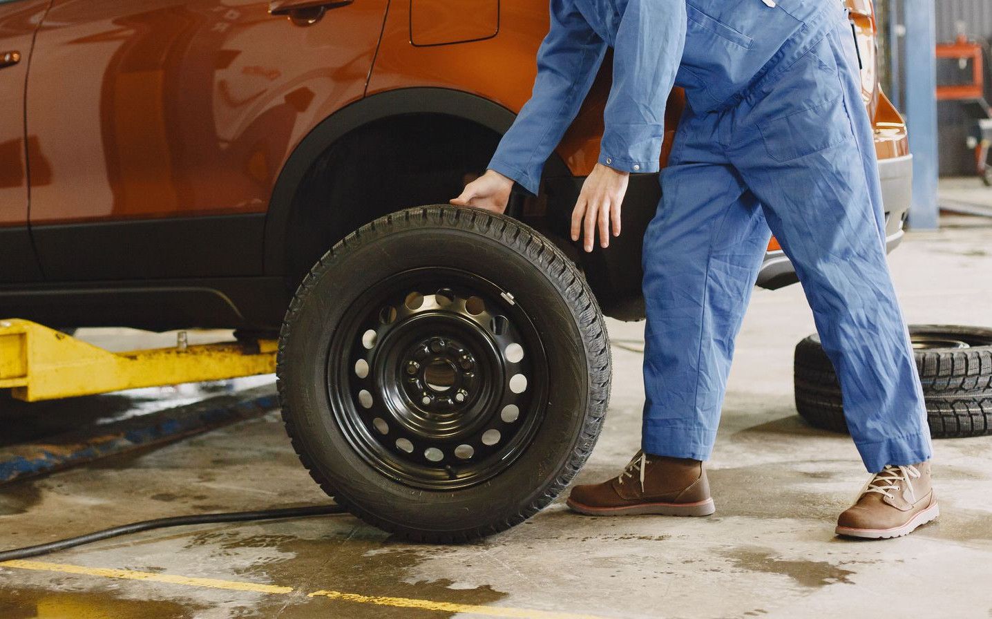 Mechanic in blue coveralls replacing tire on red SUV in repair shop garage.